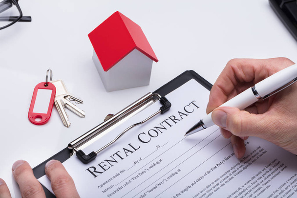 Human Hand Filling Rental Contract Form With House Model And Key On Desk - Фото, изображение