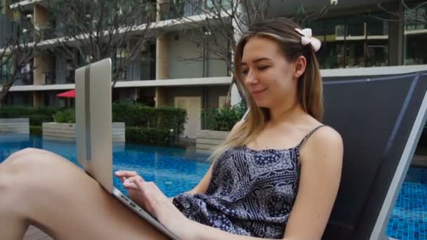 Young woman lying in beach chair and using laptop near swimming pool - Video, Çekim