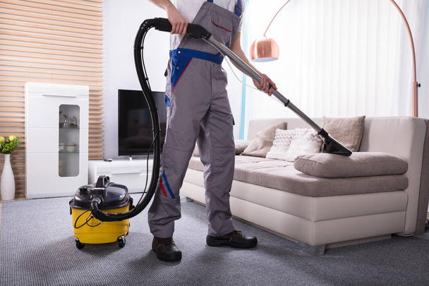 Man Cleaning Sofa In The Living Room Using Vacuum Cleaner At Home - 写真・画像