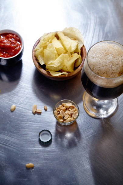 stout beer in glass with snacks and sauce in bowl on metallic background - Fotó, kép