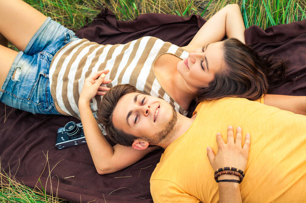 loving couple lying down with camera on blanket in floral field at warm sunny day, happiness and love concept - Fotó, kép