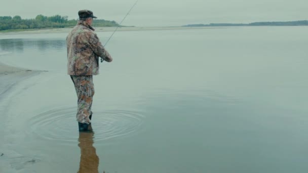 ein Fischer mit einer Zigarette ging der Fischer in Stiefeln ins Wasser und warf die Spinnerei weit in den Fluss  - Filmmaterial, Video