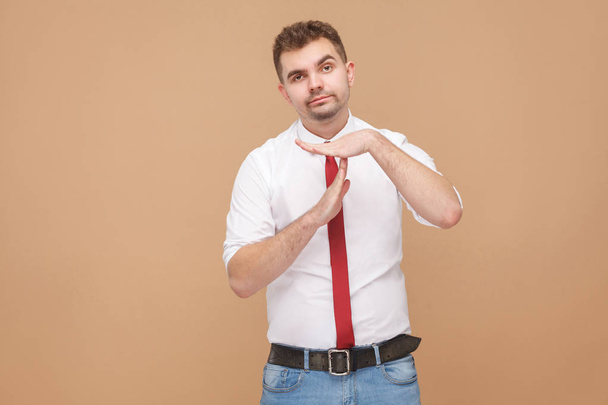 well dressed businessman showing time out sign at camera on light brown background - Fotó, kép