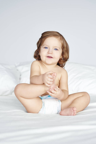Girl in diaper sitting on bed  - Фото, изображение