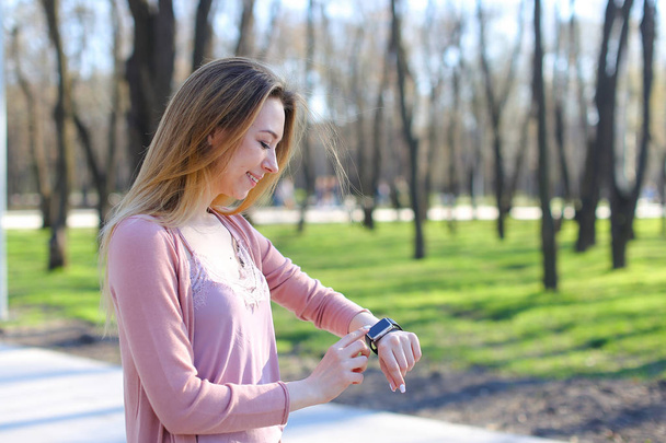 Dziewczyna spaceru w parku i przy użyciu inteligentny zegarek. - Zdjęcie, obraz