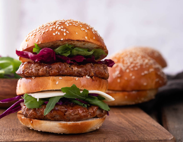 Zelfgemaakte klassieke rundvlees hamburger met dubbele patty, kaas, sla, ui, tomaat en saus op een houten achtergrond. Heerlijk eten - Foto, afbeelding