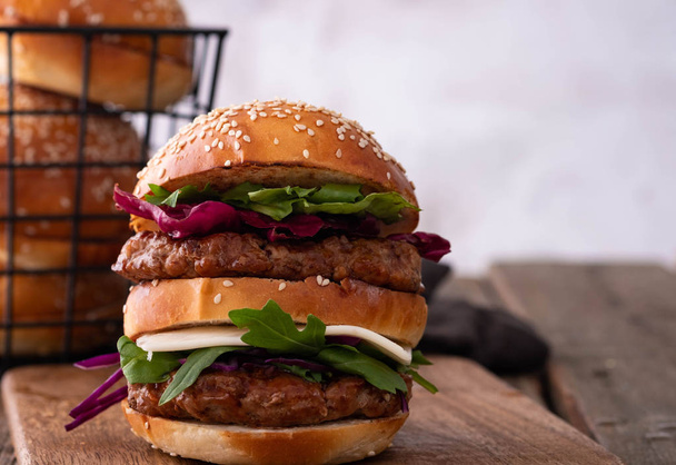 Homemade classic beef burger with double patty, cheese, lettuce, onion, tomato and sauce on a wooden background. Delicious food - Zdjęcie, obraz