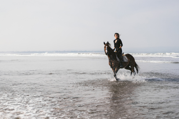 young female equestrian riding horse in water  - Foto, Bild