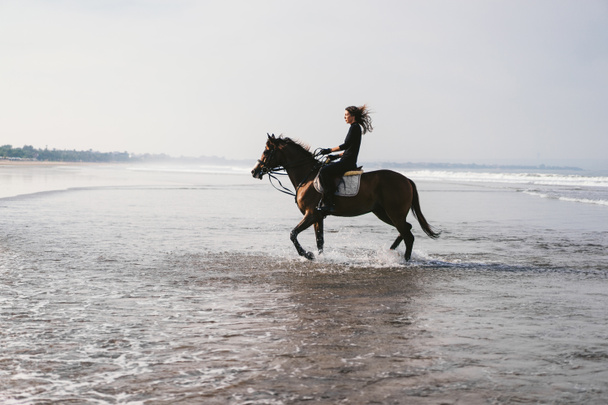 young female equestrian riding horse in water  - Photo, Image