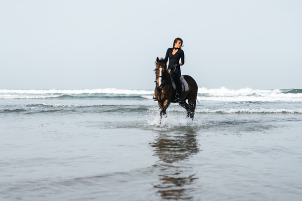 ウェーブのかかった水で馬に乗って若い女性のフロント ビュー  - 写真・画像