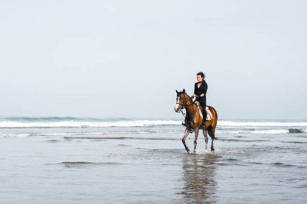 θηλυκό ιππασίας ιππασίας με τα άλογα στο νερό κυματιστό  - Φωτογραφία, εικόνα