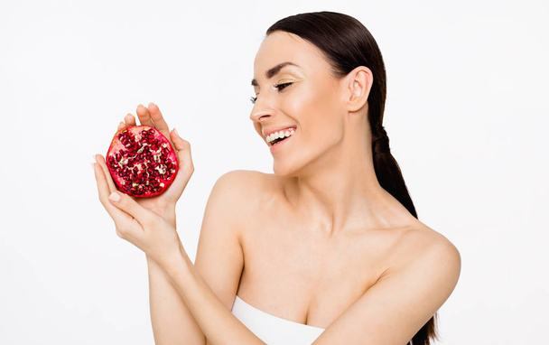 Happy and smiling beautiful woman with clean skin holding pomegranate in  hands and having fun. Fruit health. Skin and body care. - Photo, Image