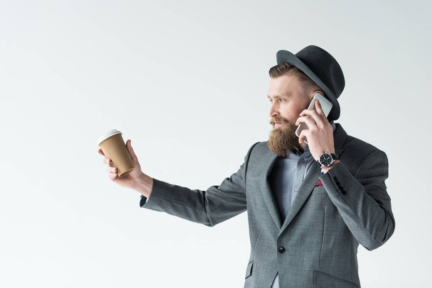 Businessman with vintage mustache and beard holding paper cup and talking on phone isolated on light background - Foto, Imagem