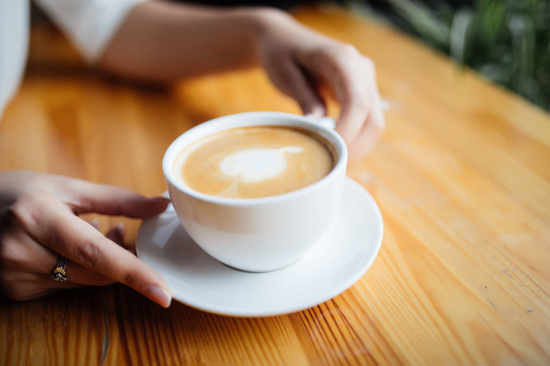Close up of female hands holding cup of coffee in cafeteria - Zdjęcie, obraz