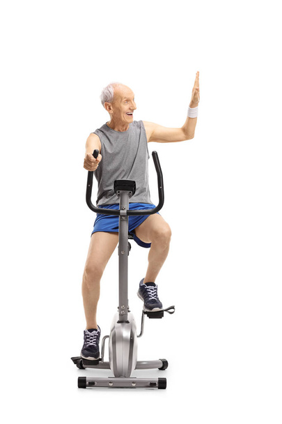 Senior exercising on a stationary bike making a high-five gesture isolated on white background - Фото, изображение