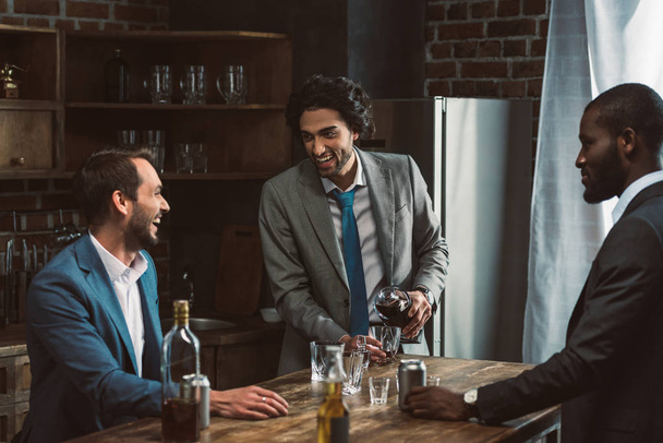 cheerful young male friends drinking alcohol beverages and talking while partying together  - Foto, Bild