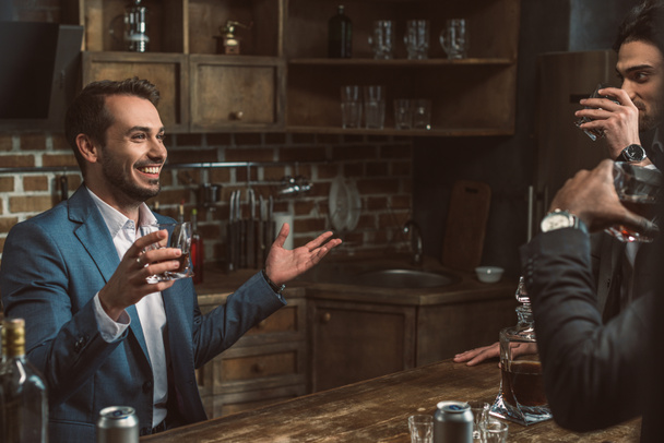 kırpılan kadeh viski içme ve birlikte konuşurken elbiseli genç adamlar - Fotoğraf, Görsel