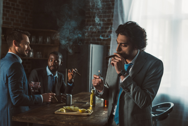 handsome young businessman smoking cigar while friends drinking whiskey behind  - Photo, Image