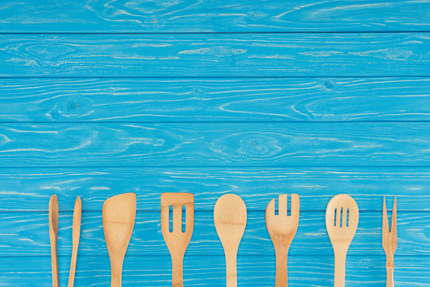 top view of wooden kitchen utensils placed in row on blue table  - Foto, Imagem