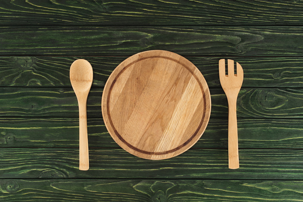 top view of round cutting board between fork and spoon on wooden table  - Photo, Image