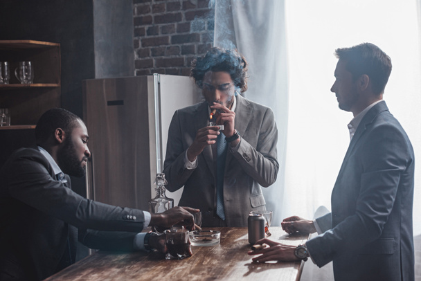 young multiethnic businessmen smoking cigars and drinking alcohol together - Photo, Image