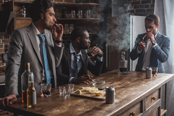 young multiethnic businessmen smoking cigars and drinking alcohol while partying together - Photo, Image