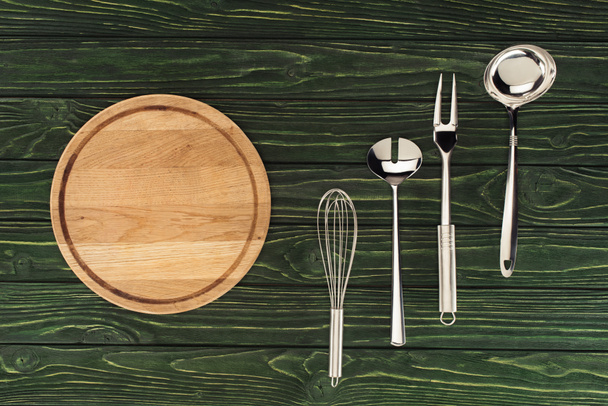 Draufsicht auf rundes Holzschneidebrett und metallische Küchenutensilien auf dem Tisch  - Foto, Bild
