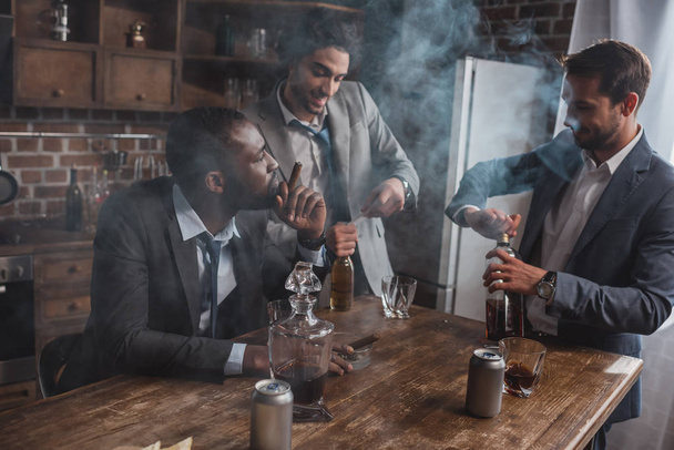 young multiethnic businessmen smoking cigars and drinking alcoholic beverages - Fotografie, Obrázek