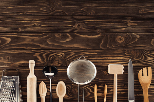 elevated view of kitchen utensils placed in row on wooden table - Foto, afbeelding