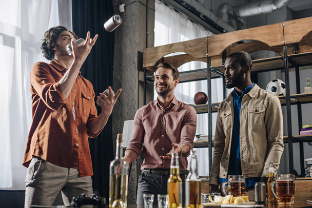 vue à angle bas d'hommes multiethniques regardant un ami jongler avec des canettes de bière
 - Photo, image