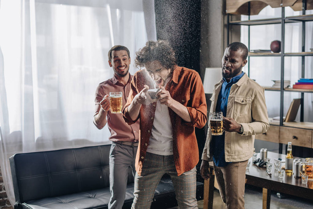 сміються багатоетнічні друзі, дивлячись на людину, яка п'є пиво з банки
  - Фото, зображення