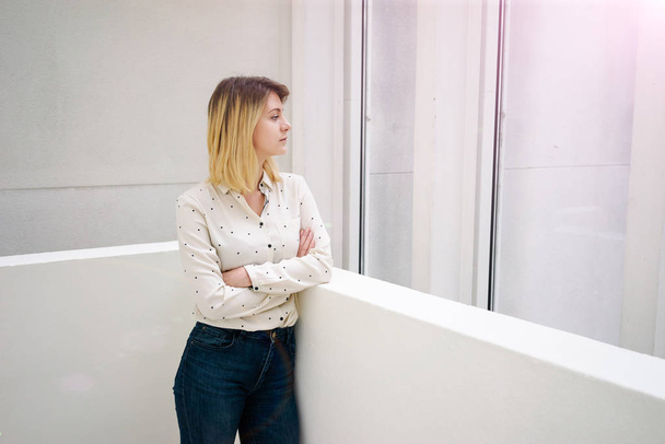 Young blonde businesswoman thinking about something while standing in modern office interior - Foto, Imagem