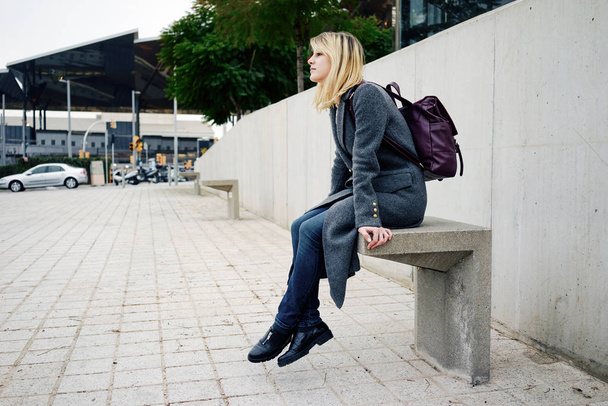 portrait of a young beautiful woman with blonde hair sitting against gray concrete wall - Photo, image