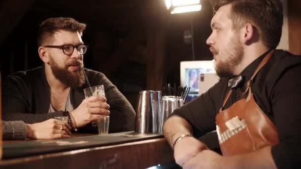 Bebaarde man praat met de barman in een bar in de avond, close-up - Video