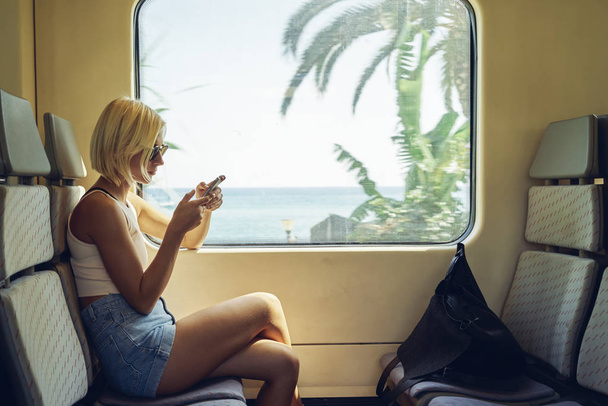young woman using smartphone in a moving train near window - 写真・画像