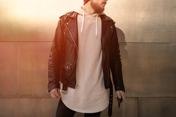 Young man wearing white blank sweatshirt and leather jacket standing on a metal wall background - Foto, immagini