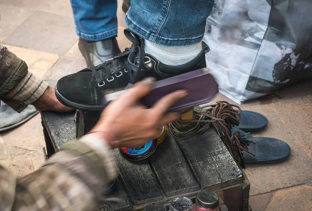 ο άνθρωπος τον καθαρισμό πελάτη παπούτσια στο πεζοδρόμιο της πόλης. - Φωτογραφία, εικόνα