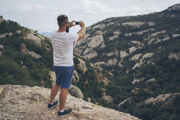 Male hiker is taking photo by smartphone on the peak of mountain. - Photo, Image