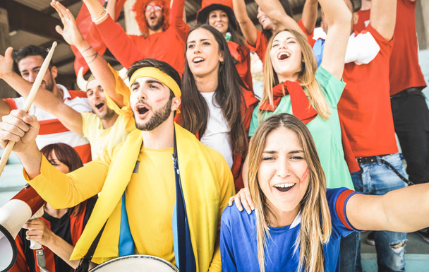 Junge Fußballfans jubeln und gucken Pokalspiel im Stadion - Fangruppe mit bunten T-Shirts begeistert vom WM-Konzept - Foto, Bild