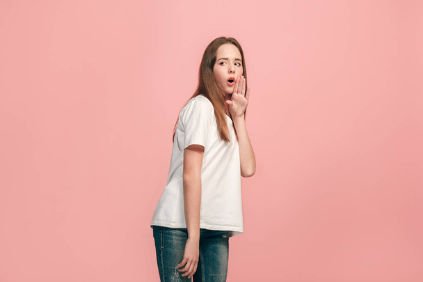 The young teen girl whispering a secret behind her hand over pink background - Foto, imagen