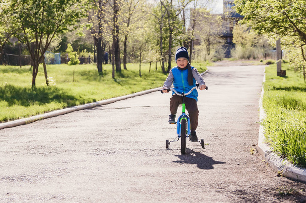 five year old boy in a blue vest riding a bike in a spring Park - Fotografie, Obrázek