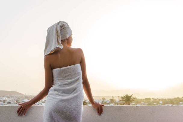 girl on the terrace in a bath towel after the shower looks at the sunset in the mountains - Foto, afbeelding