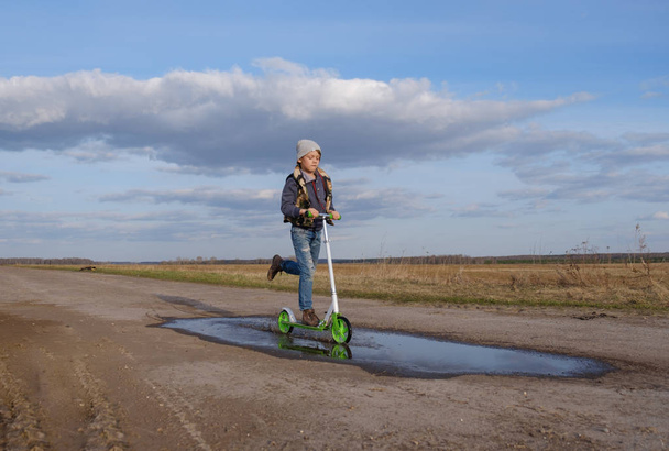 European boy rides his scooter through the puddles - Foto, imagen