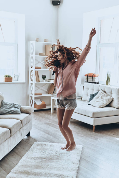 happy woman in pajamas singing and dancing in modern apartment - Fotó, kép