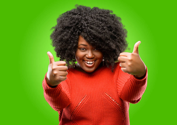 Hermosa mujer africana sonriendo ampliamente mostrando pulgares hacia arriba gesto a la cámara, expresión de gusto y aprobación
 - Foto, imagen