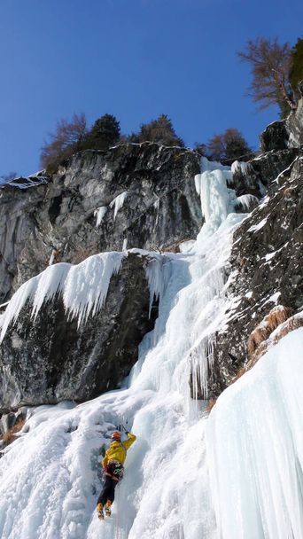 гид поднимается на крутой замерзший водопад в холодный зимний день в Альпах
 - Фото, изображение