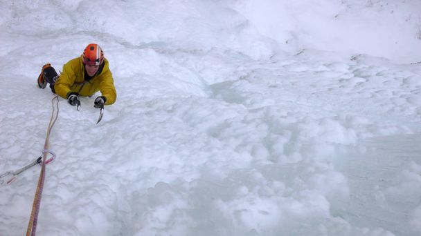 mannelijke berggids klimmen een steile bevroren waterval op een koude winterdag in de Alpen - Foto, afbeelding