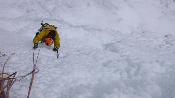 Bergführer besteigt an einem kalten Wintertag in den Alpen einen steilen gefrorenen Wasserfall - Foto, Bild