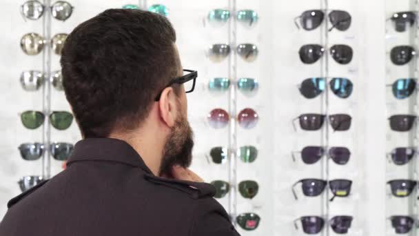 Close up tiro de um homem dountful escolher óculos de sol na loja
 - Filmagem, Vídeo