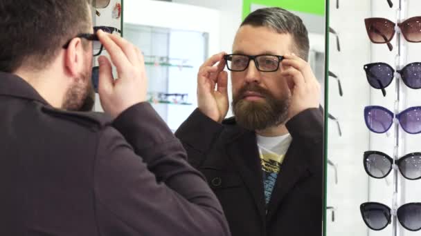 Зрілий чоловік намагається на нових окулярах спереду, якщо дзеркало в магазині
 - Кадри, відео